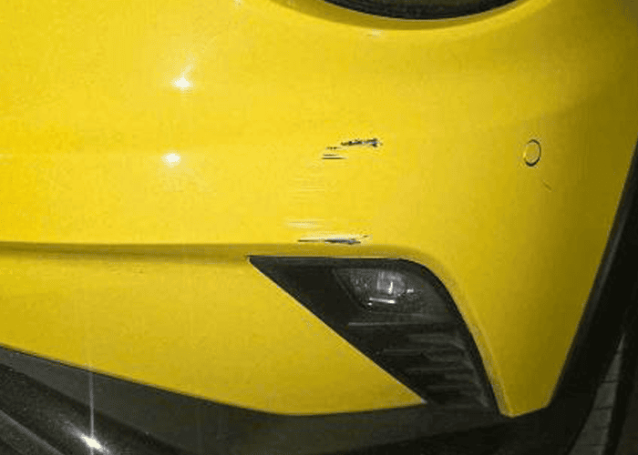 Minor scratches and scuffs on a yellow car bumper before cosmetic repair